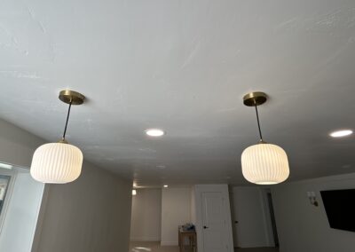 Two white pendant lights with brass fixtures hang from a white ceiling in a modern room with recessed lighting and neutral walls.