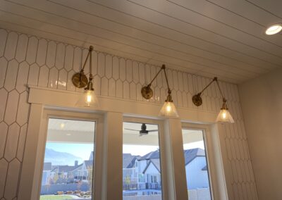 Four wall-mounted brass and glass sconce lights are installed above two large windows on a tiled wall in a modern interior.
