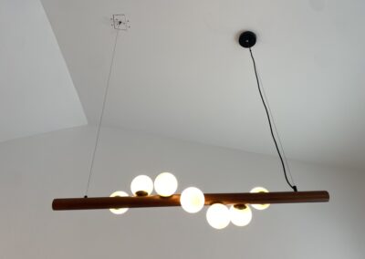 A modern light fixture with round bulbs hangs from the ceiling on two cables, with a visible black power cord trailing to a ceiling mount.