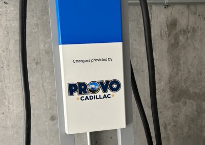 Ultium Charge 360 electric vehicle charging station with signage indicating chargers provided by Provo Cadillac, set against a concrete wall background.