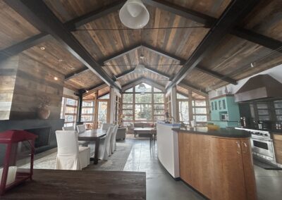 Open-concept living and dining area with wood-paneled vaulted ceiling, large windows, modern kitchen, and natural light filling the space.